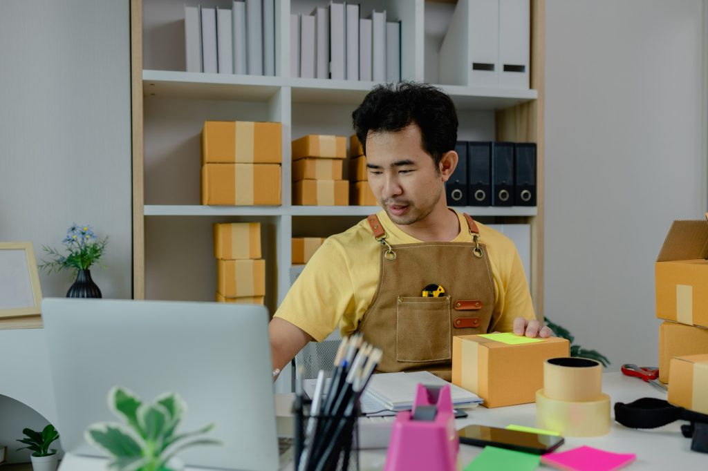 An entrepreneur is checking products in the system and packing them up to ship to buyers from his on