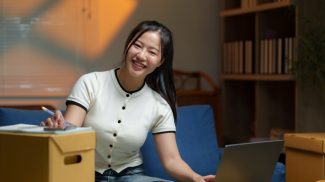 Asian woman managing inventory and logistics using laptop at home