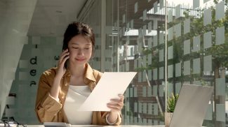Charming Asian woman with a smile standing holding papers and mobile phone at the office.