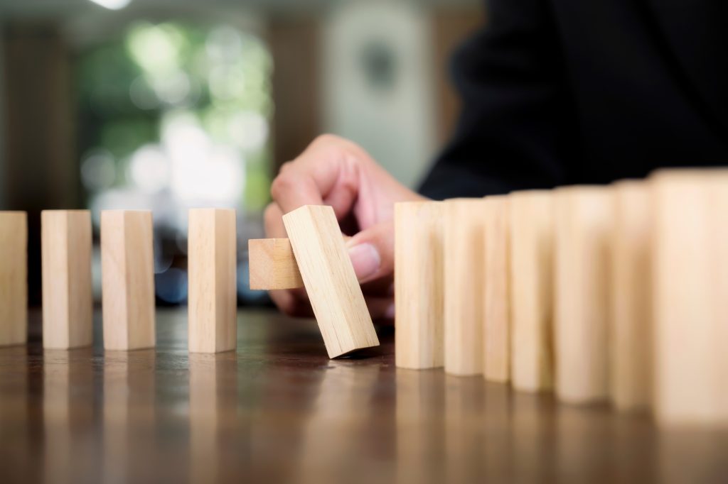 Close up of businessman hand Stopping Falling wooden Dominoes