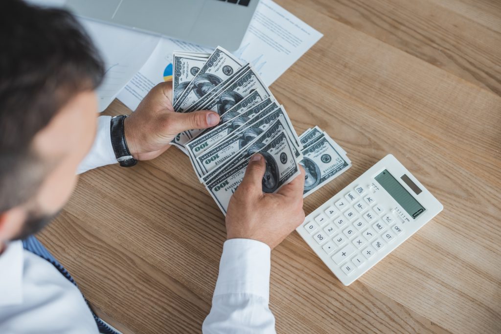 cropped image of financier counting cash with calculator in office