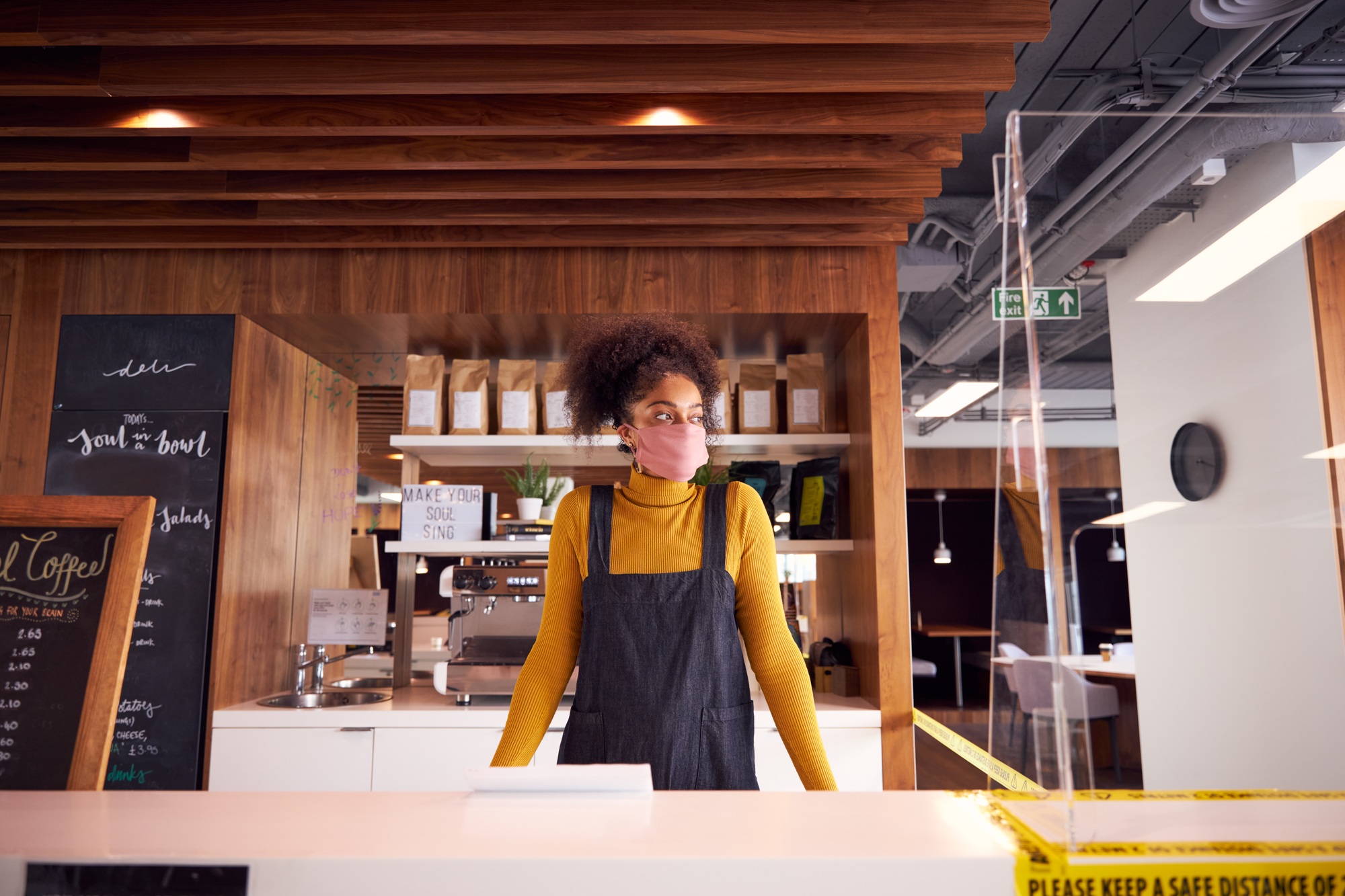 Female Small Business Owner Of Coffee Shop In Mask Standing Behind Counter During Health Pandemic
