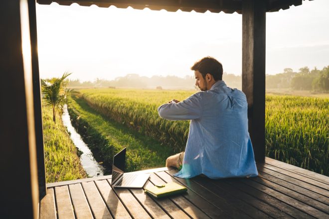 Focused young man checking wristwatch while working remotely in countryside
