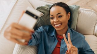 Happy African American woman holding mobile phone, using mobile app, influencer recoding video