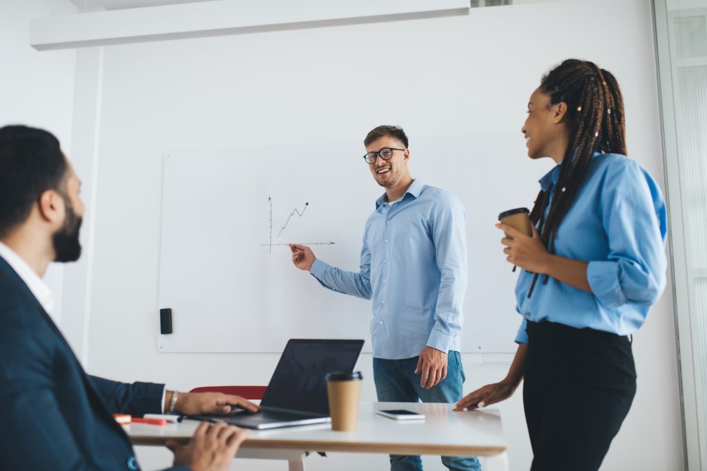 Happy professional employee in glasses explaining infographics charts in board room