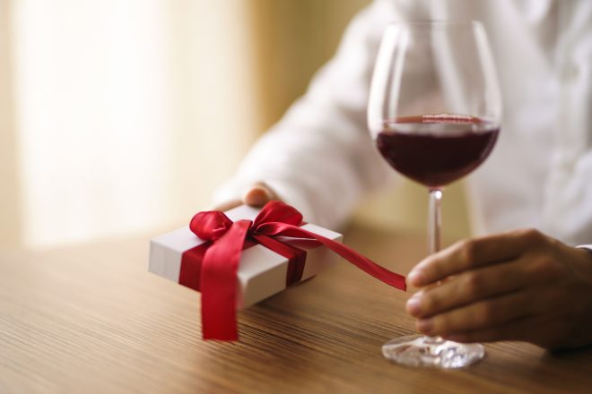 Man's hands with glass of wine and gift. Present with red ribbon. male hands hold surprise gift box.