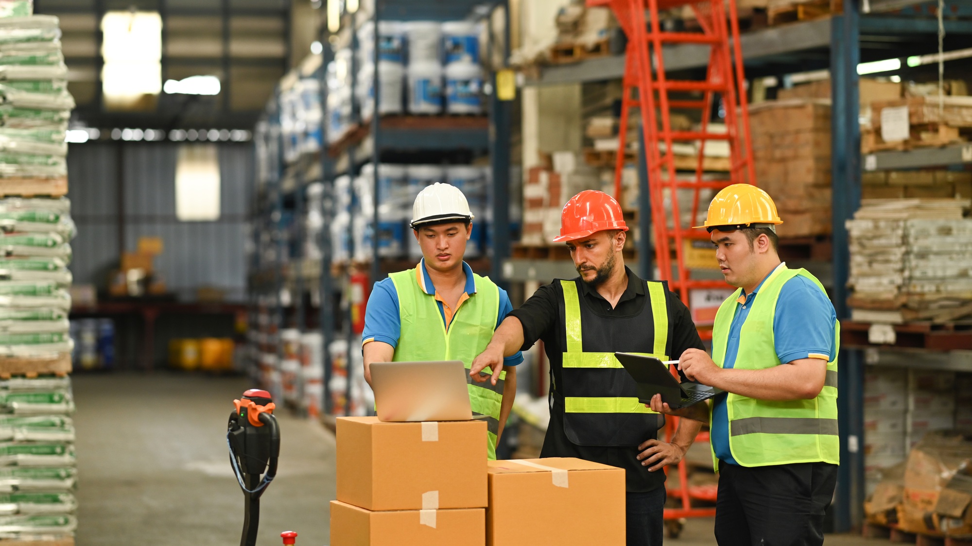 Manager and warehouse worker inspecting stock tick and cardboard stock product on laptop.
