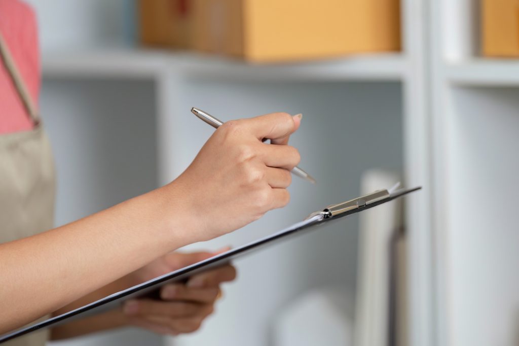Small Business Management. A woman taking notes while checking inventory.