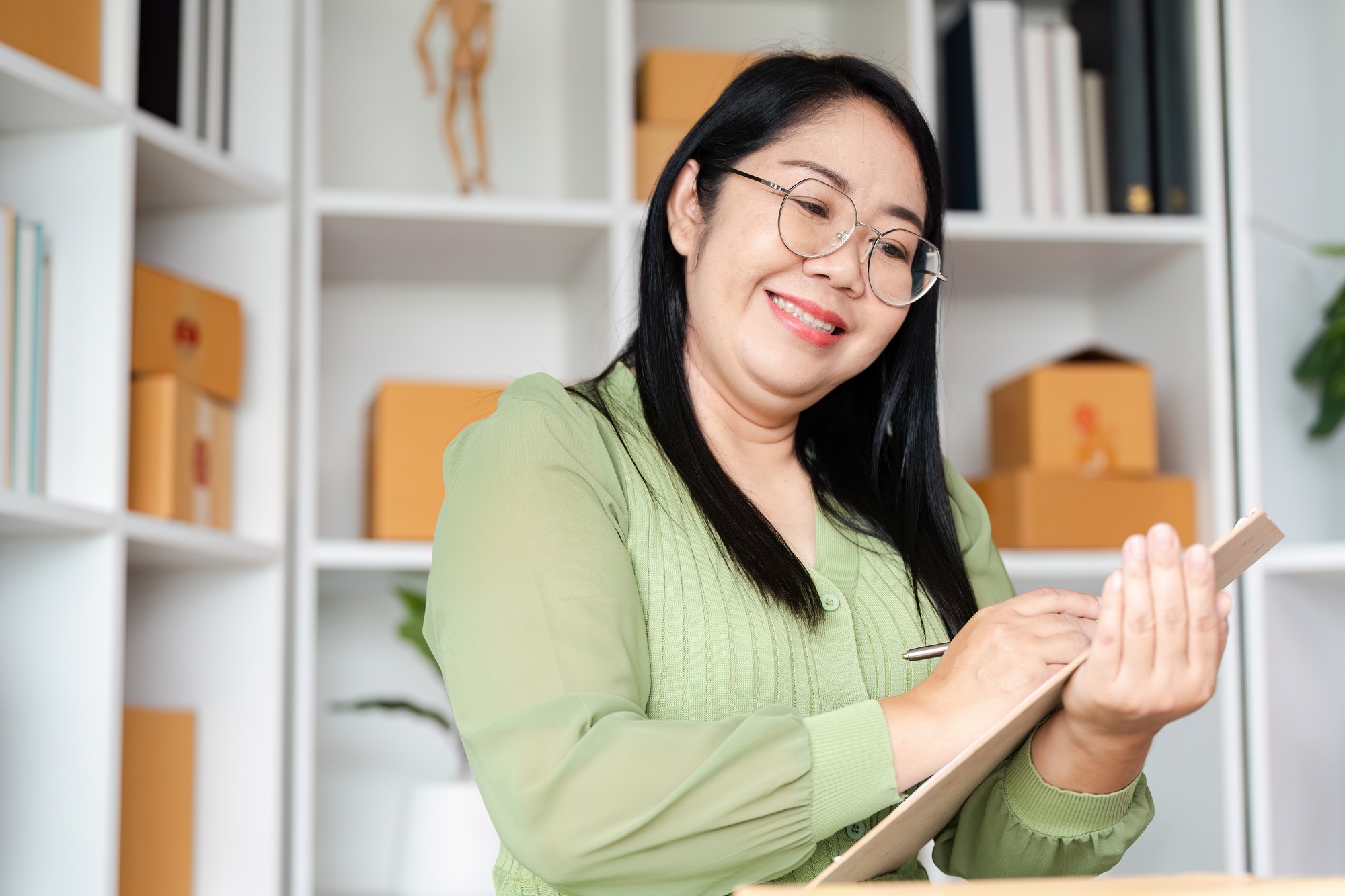Smiling Woman Managing Inventory in Small Business Office with Shelves and Boxes
