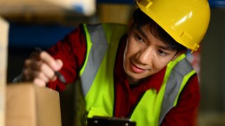 Storehouse worker checking stock and inventory on clipboard.