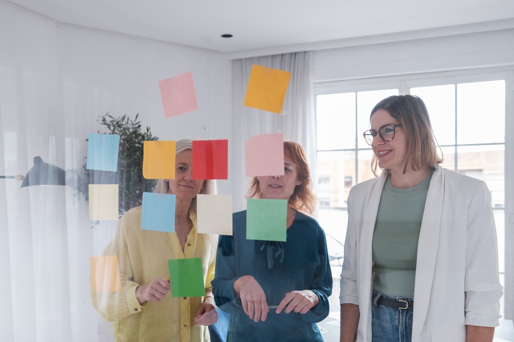 The three members of a start up discussing and collecting ideas on a transparent board.