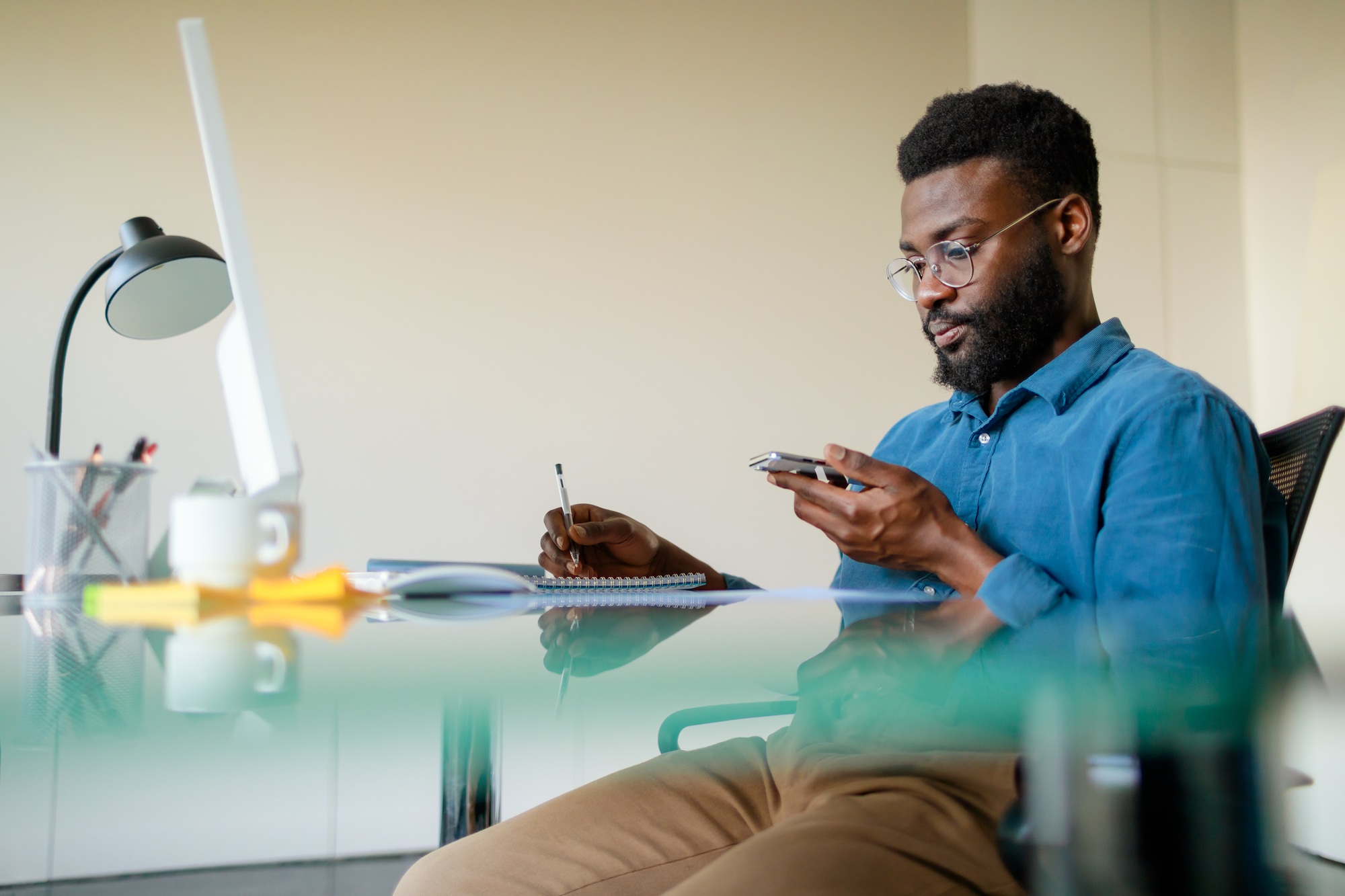 Time management concept. Serious black businessman using cellphone and taking notes, working in