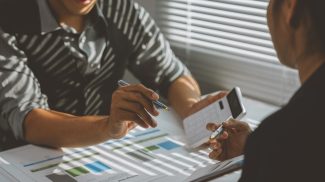 Two business people are discussing financial charts and using a calculator, analyzing business growt