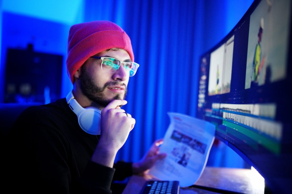 Young man editing video with a focused expression in a dimly lit room at night